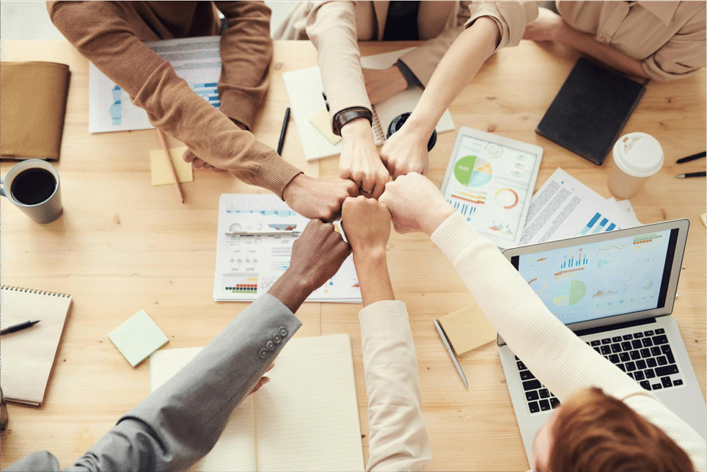 Team members doing a group fist bump over a meeting table with charts and laptops
